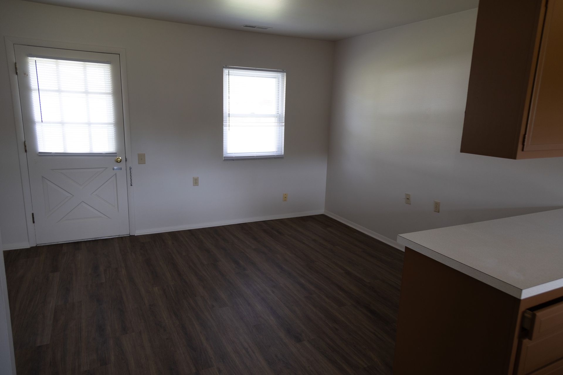 An empty living room with hardwood floors and two windows.