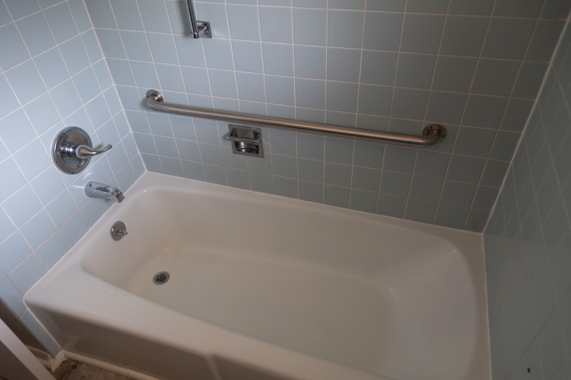 A bathtub in a bathroom with blue tiles and a hand rail.