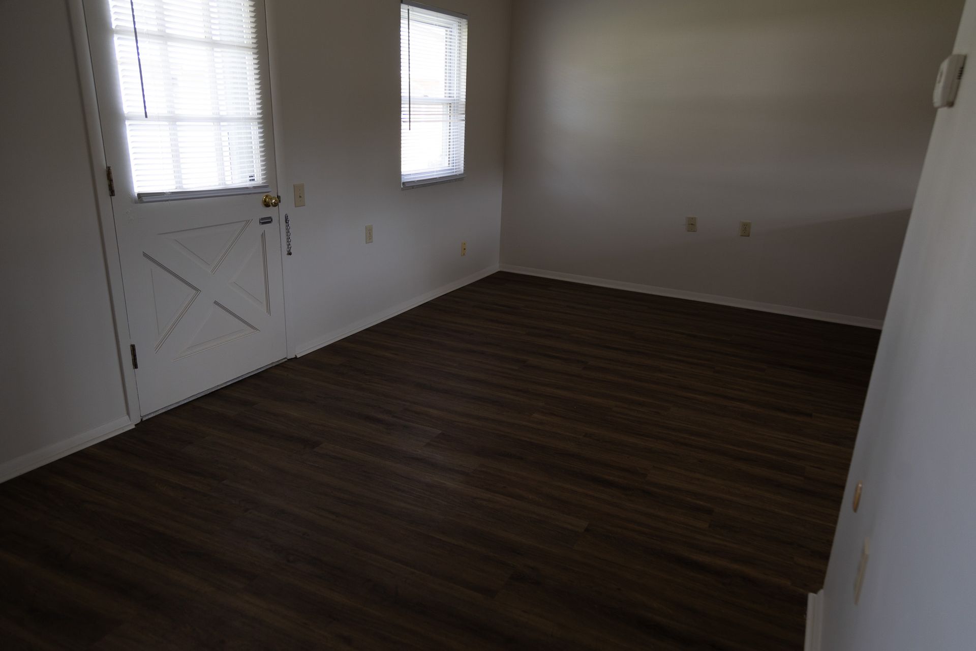 An empty living room with a wooden floor and white walls.