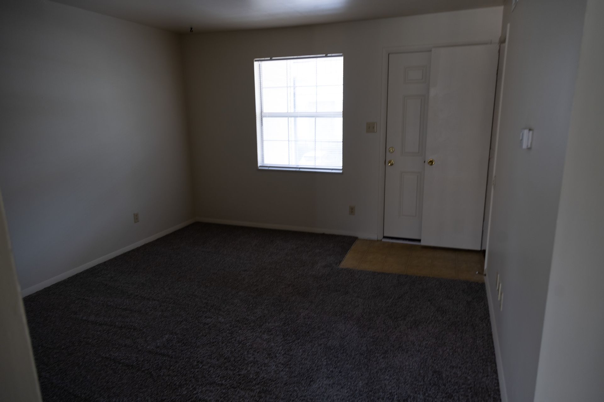 An empty living room with a window and a door.