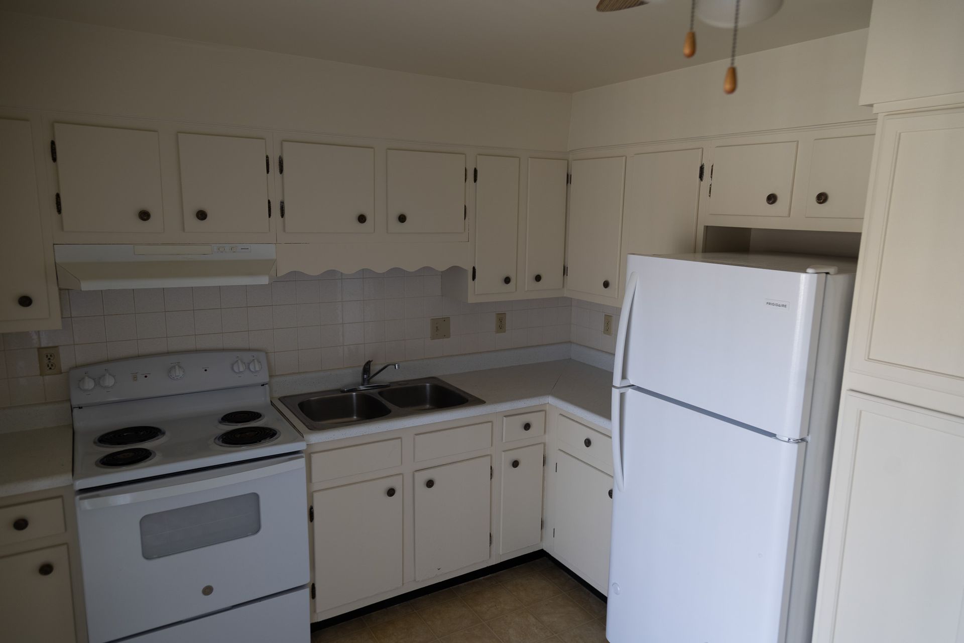 An empty kitchen with white cabinets and a white refrigerator