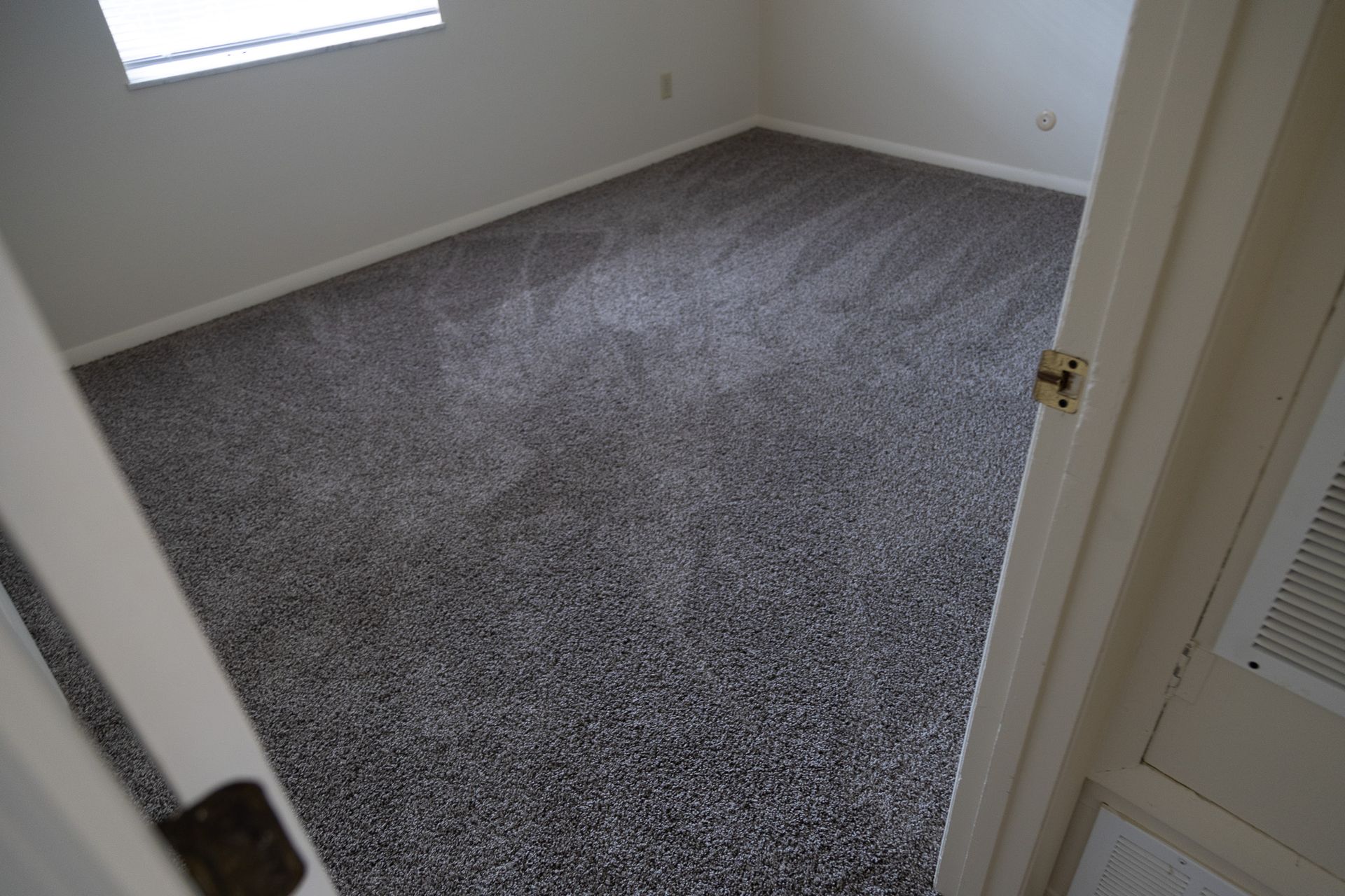 A bedroom with a carpeted floor and a window.