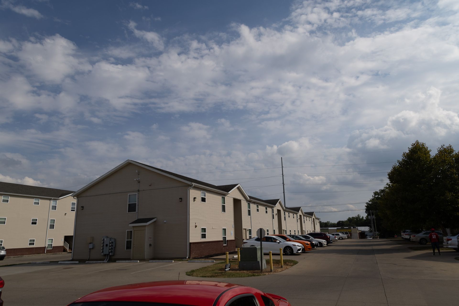 A red car is parked in front of a row of apartment buildings.