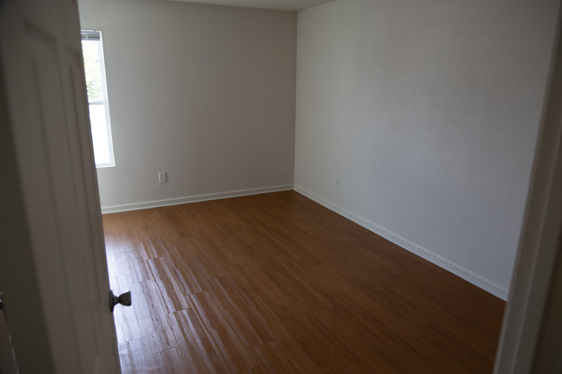 An empty bedroom with hardwood floors and white walls.
