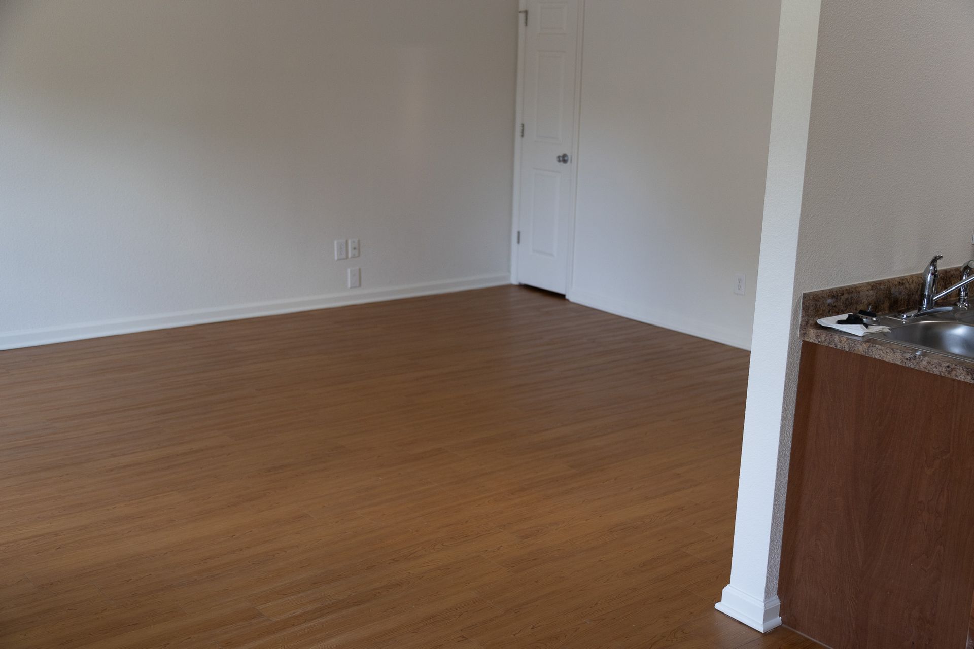 An empty living room with hardwood floors and a sink.