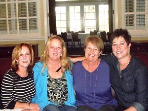 Four women are posing for a picture while sitting on a couch.