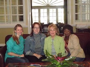 Four women are posing for a picture while sitting on a couch
