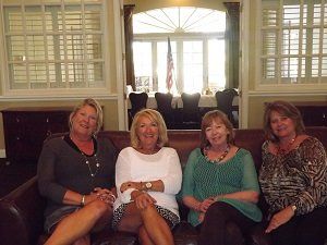 Four women are sitting on a couch and smiling for the camera