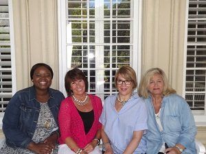 Four women are sitting on a porch in front of a window.