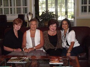 Four women are posing for a picture while sitting on a couch.