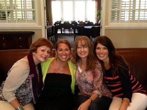 Four women are posing for a picture while sitting on a couch
