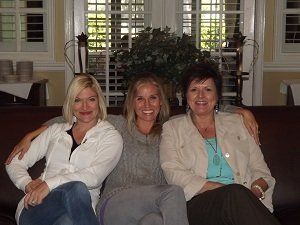 Three women are posing for a picture while sitting on a couch.