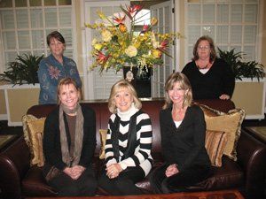 Four women are sitting on a couch in front of a vase of flowers