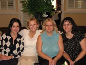 Four women are posing for a picture while sitting on a couch.
