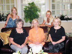 Four women are posing for a picture while sitting on a couch
