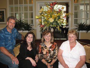 A group of people are sitting on a couch in front of a vase of flowers.