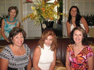 A group of women are posing for a picture in front of a vase of flowers.