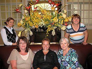 A group of women are posing for a picture in front of a vase of flowers.