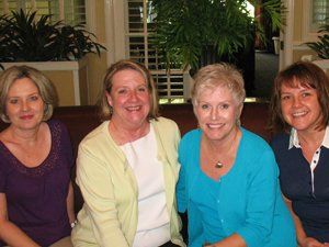 Four women are posing for a picture while sitting on a couch.