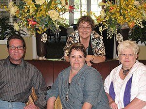 A group of people are posing for a picture in front of a vase of flowers.