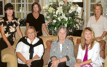 A group of women are posing for a picture in front of a vase of flowers.