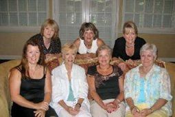 A group of women are sitting on a couch posing for a picture.