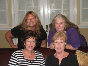 Four women are posing for a picture while sitting on a couch.