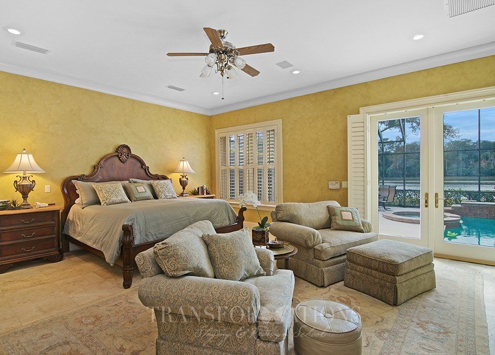 A bedroom with a bed , chairs , ottomans and a ceiling fan.