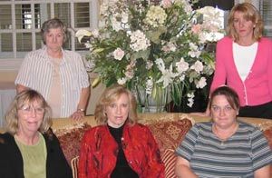 A group of women are posing for a picture in front of a vase of flowers.