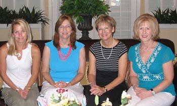 Four women are sitting on a couch and smiling for the camera