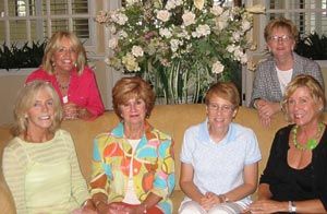 A group of women are sitting on a couch in front of a vase of flowers.