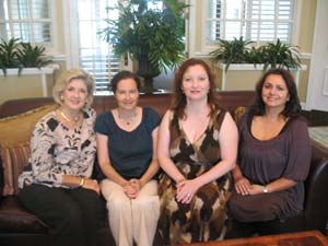 Four women are posing for a picture while sitting on a couch.