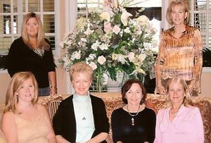 A group of women are posing for a picture in front of a vase of flowers