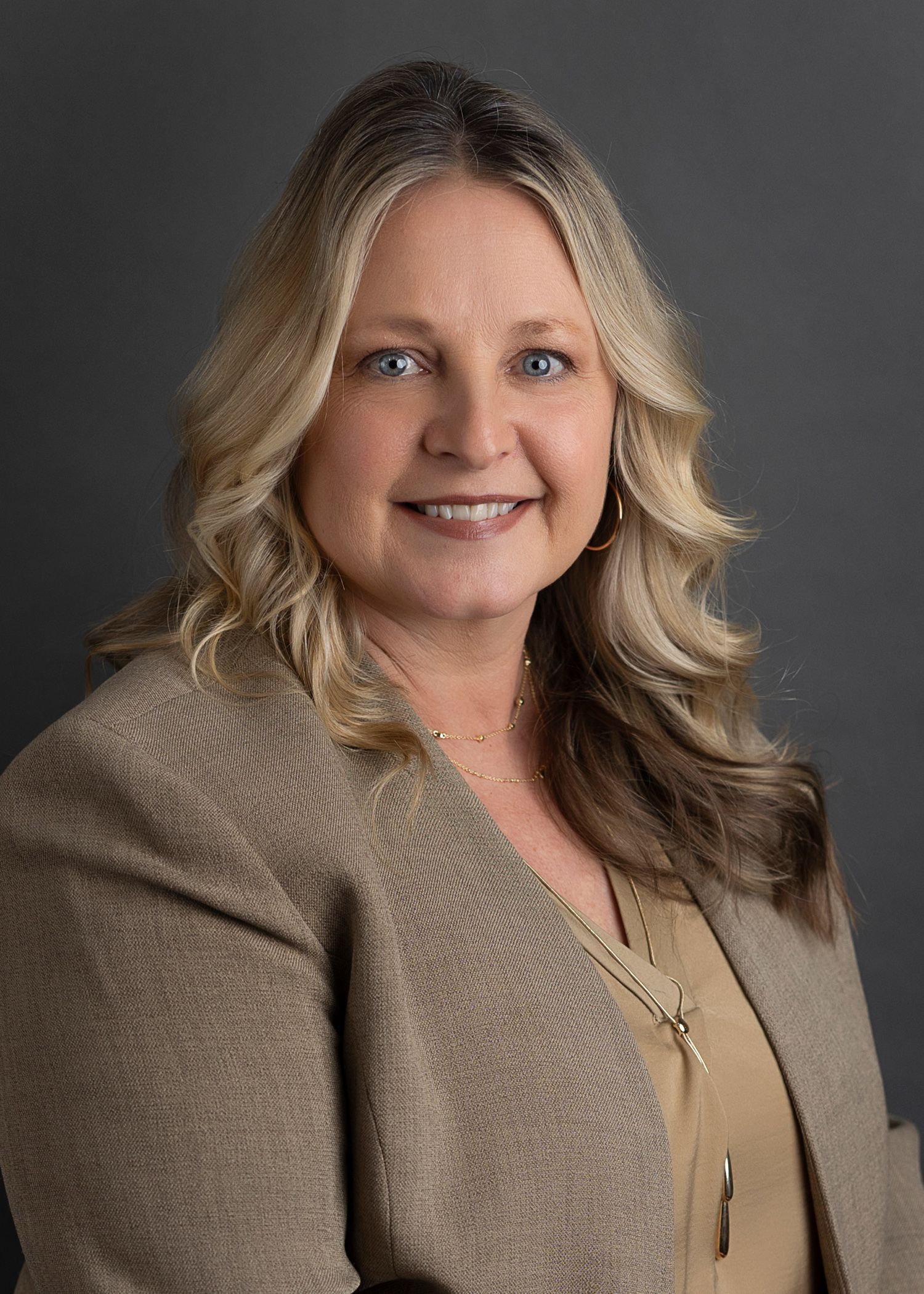 A woman wearing a blue shirt and a necklace is smiling for the camera.
