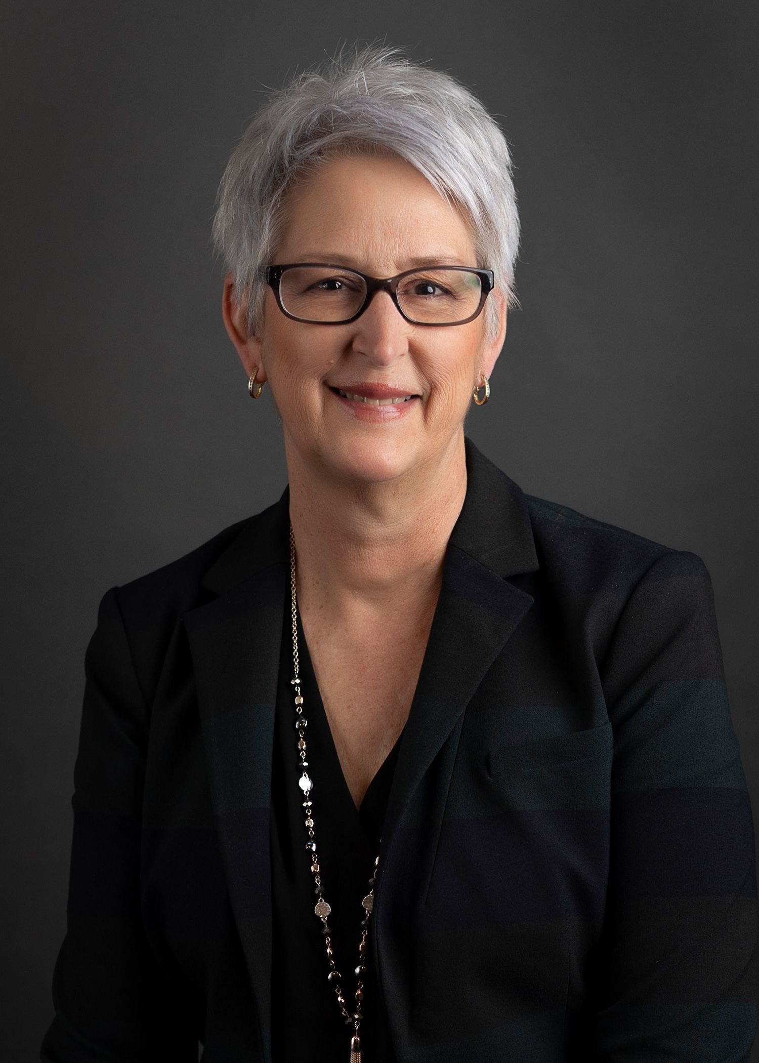 A woman wearing glasses and a necklace is smiling for the camera.