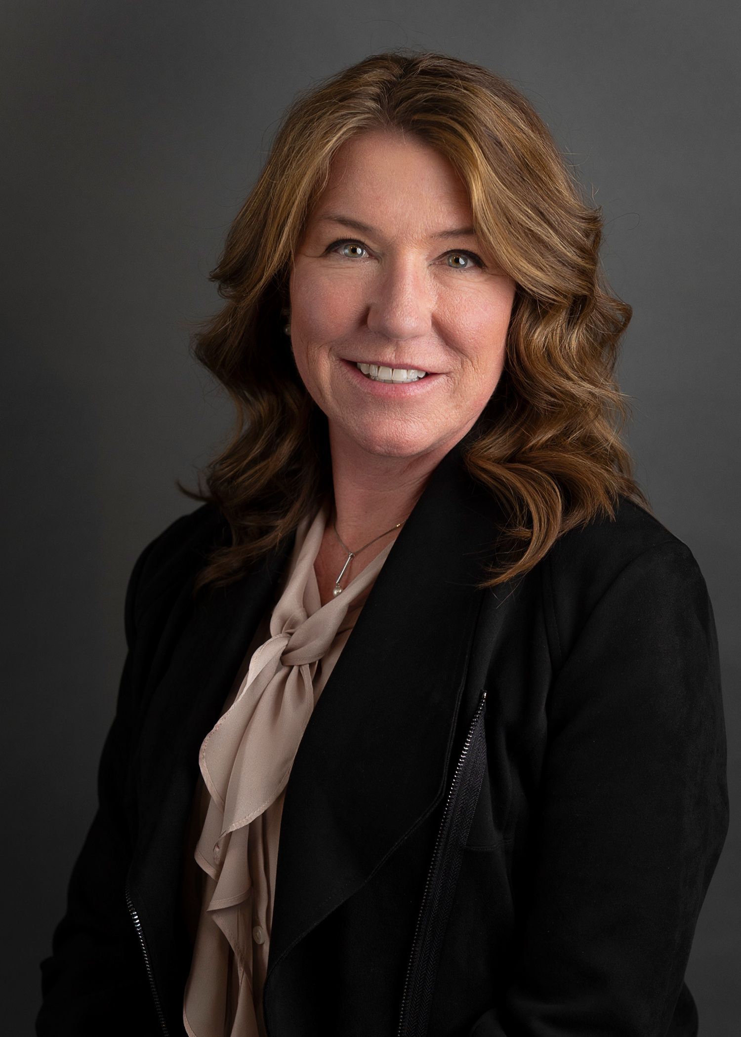 A woman wearing a black shirt and a necklace is smiling for the camera.