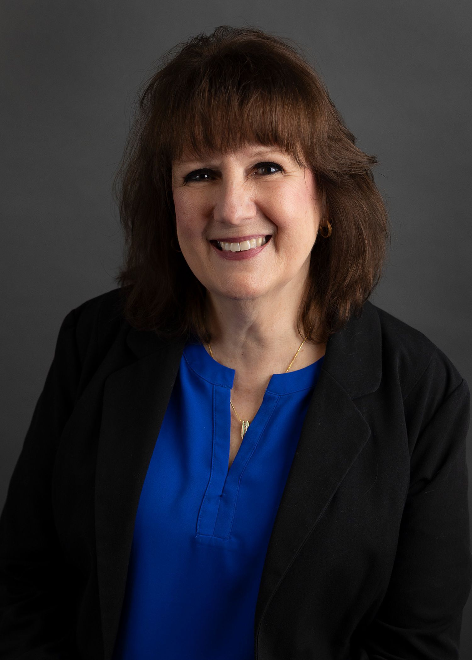 A woman wearing a purple shirt and a necklace is smiling for the camera.