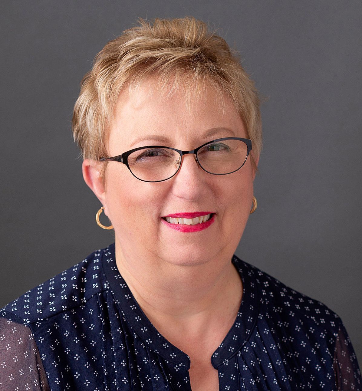 A woman wearing glasses and a blue shirt is smiling for the camera.