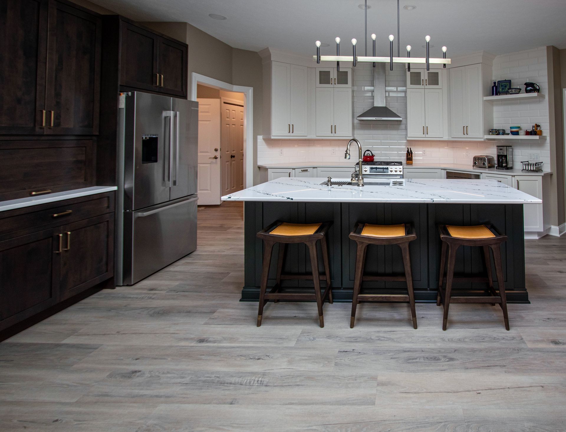 A kitchen with a large island , stools and a refrigerator.