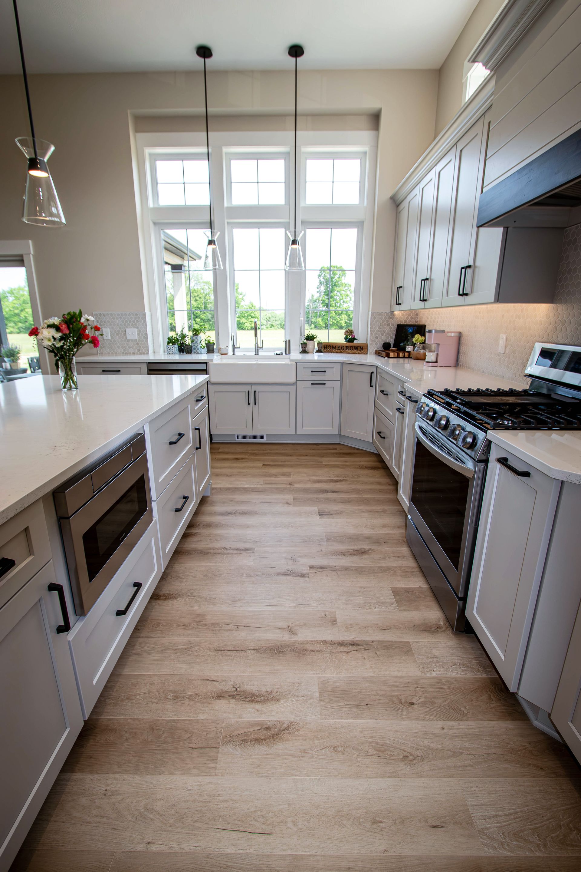 A kitchen with white cabinets , stainless steel appliances , hardwood floors and a large island.