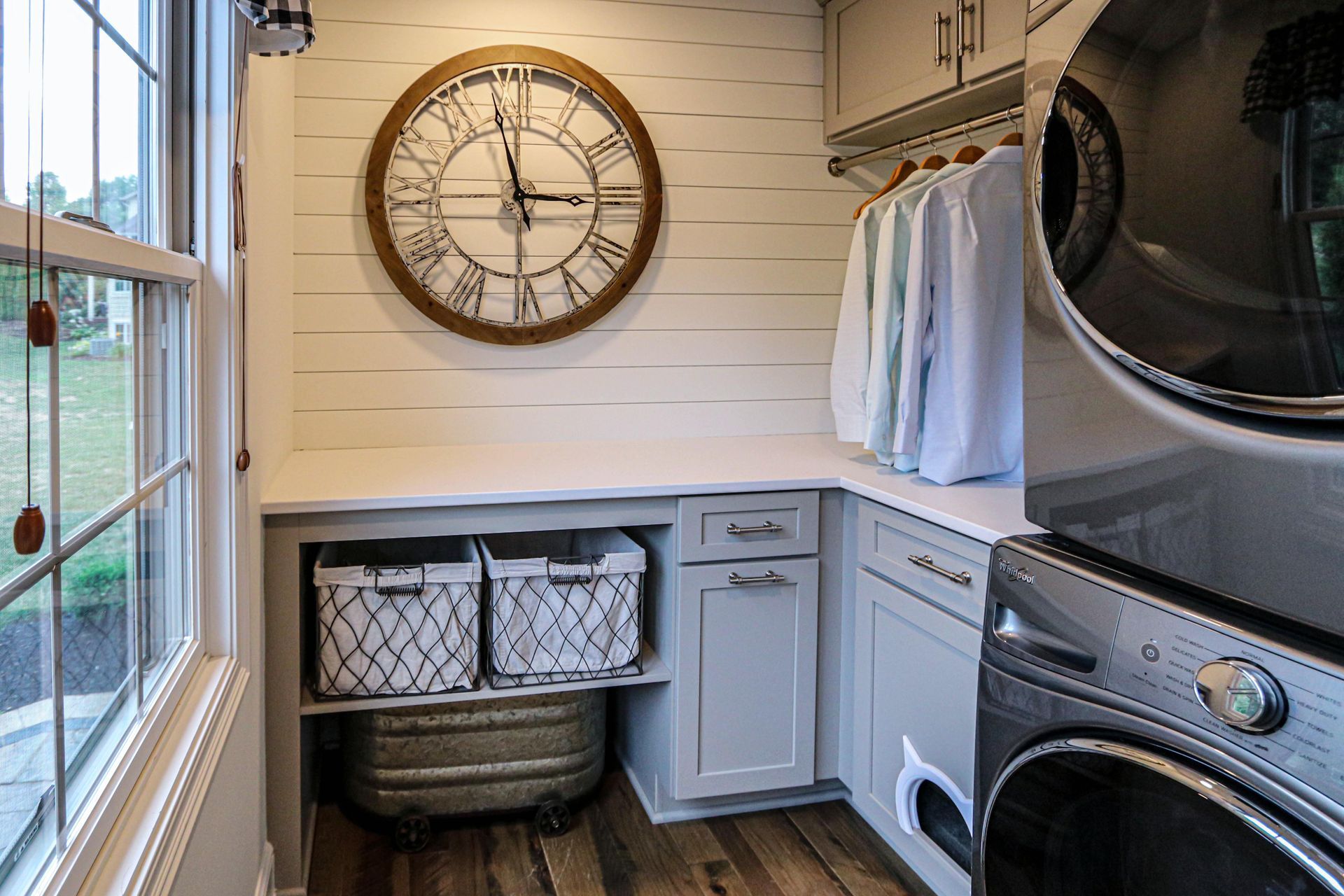 A laundry room with a clock on the wall and a washer and dryer stacked on top of each other.