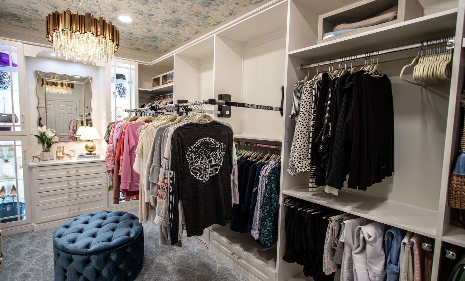 A walk in closet filled with lots of clothes and a blue ottoman.