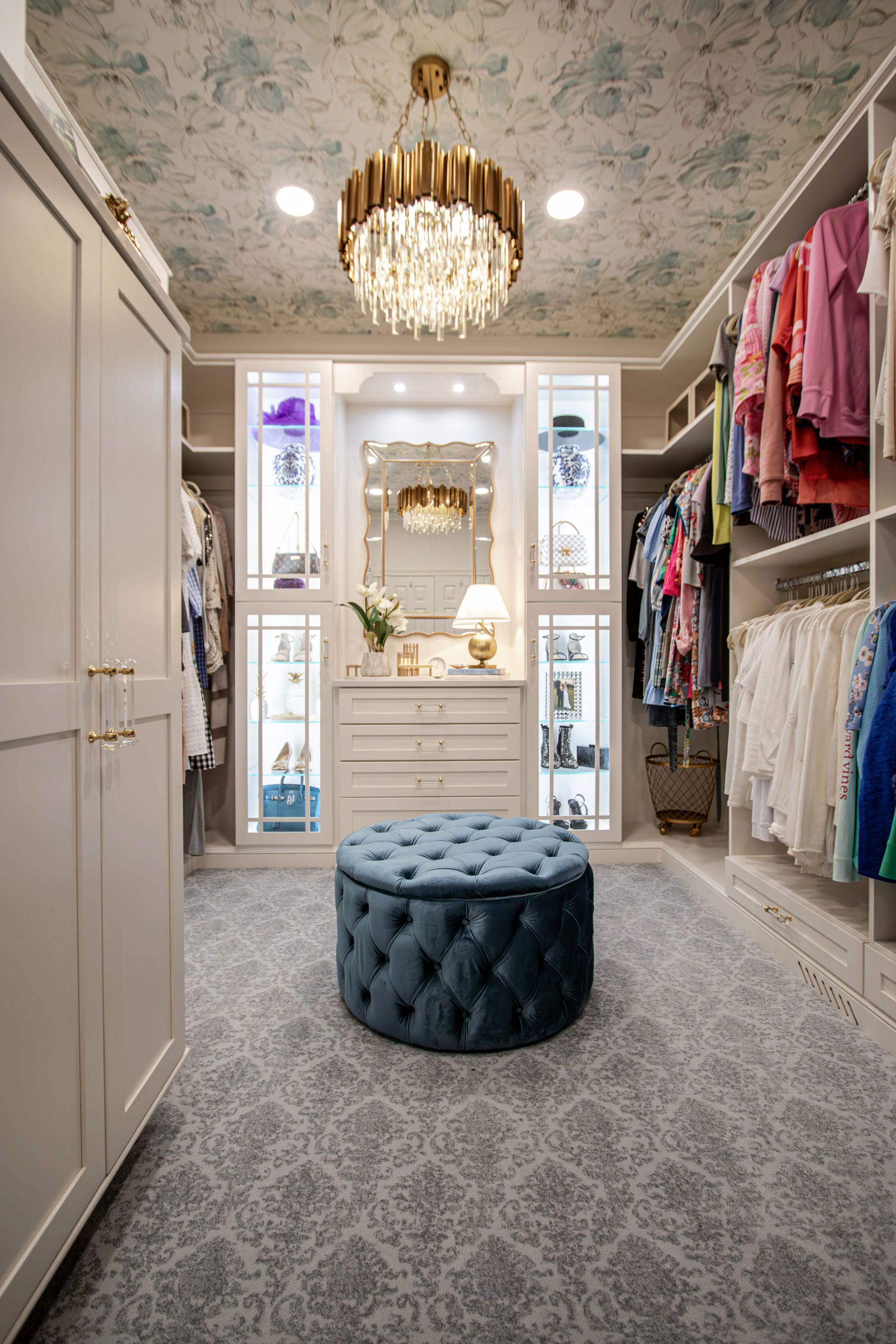 A walk in closet with a blue ottoman and a chandelier.