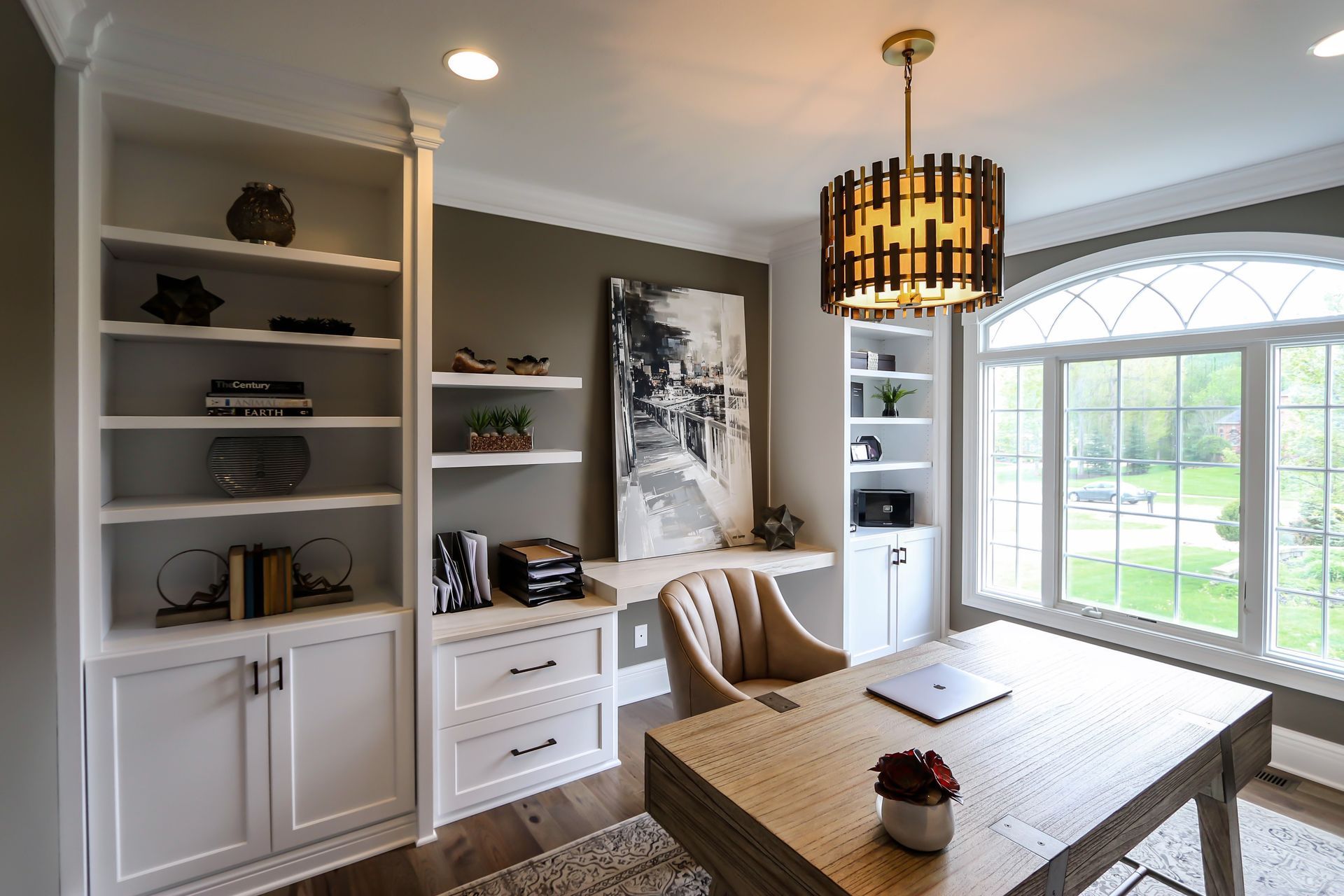 A home office with a desk , chair , shelves and a chandelier.