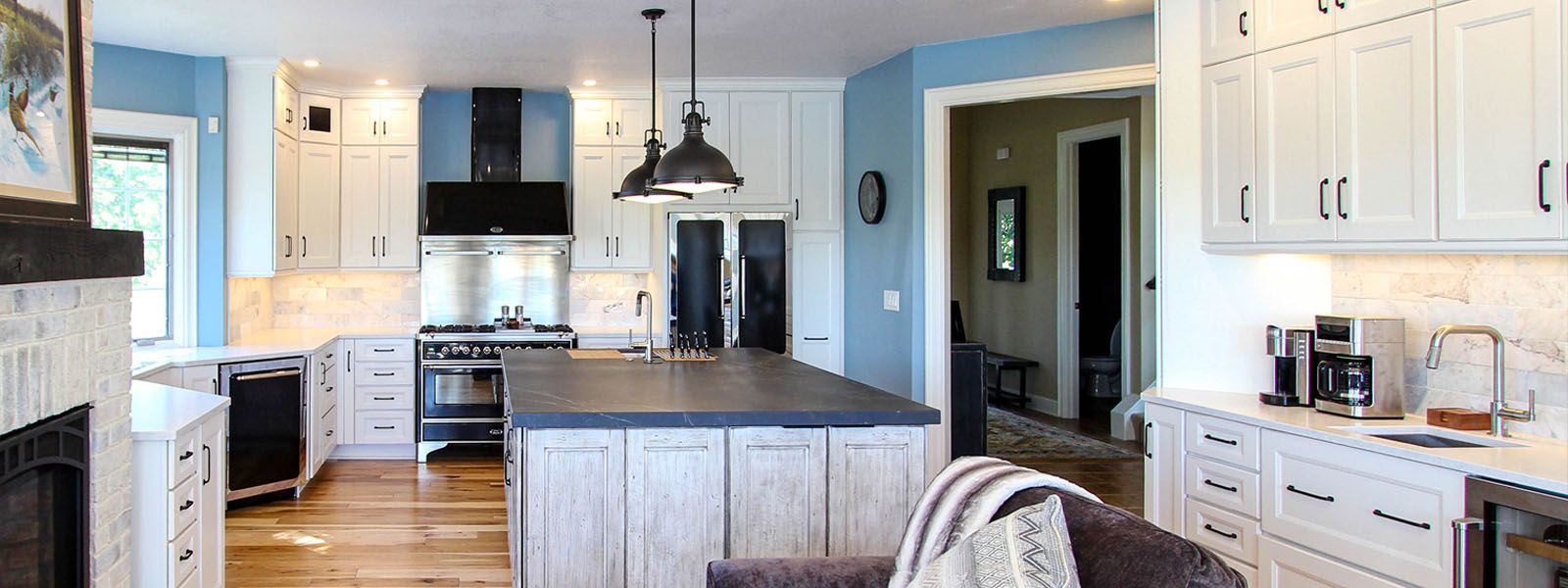 A kitchen with white cabinets , stainless steel appliances , a large island and a fireplace.