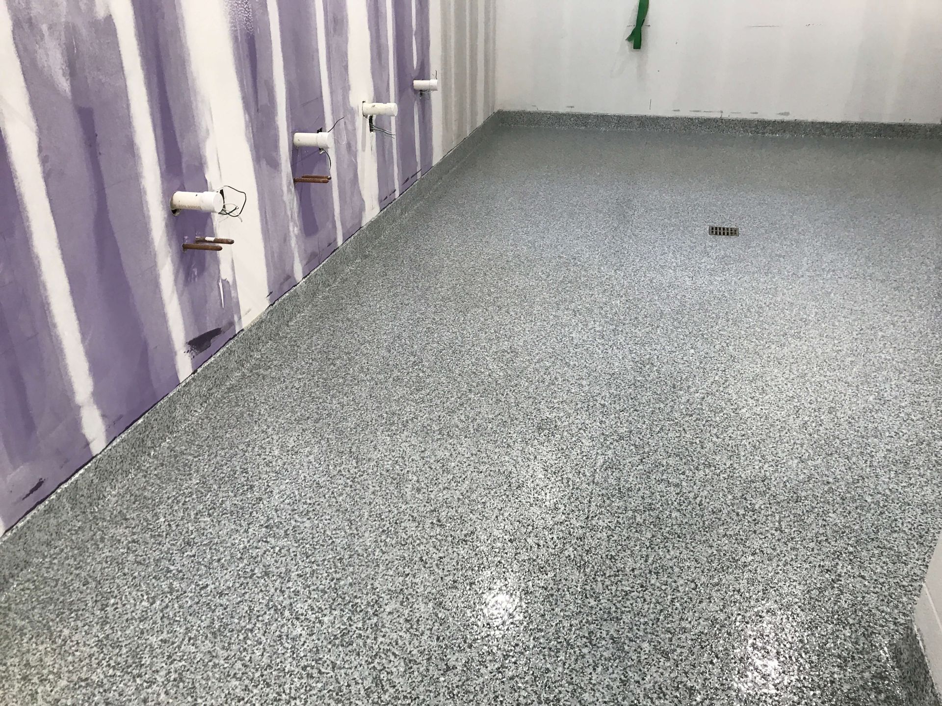 Epoxy flooring in a bathroom under construction; gray flecked pattern, drywall walls.