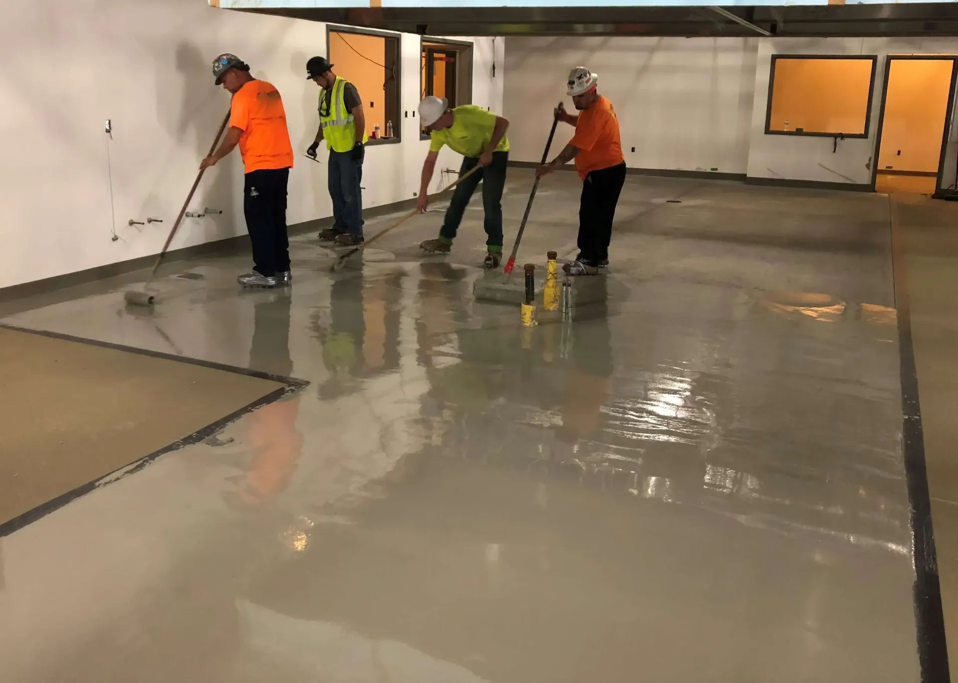 A group of men applying urethan a concrete floor in a building.