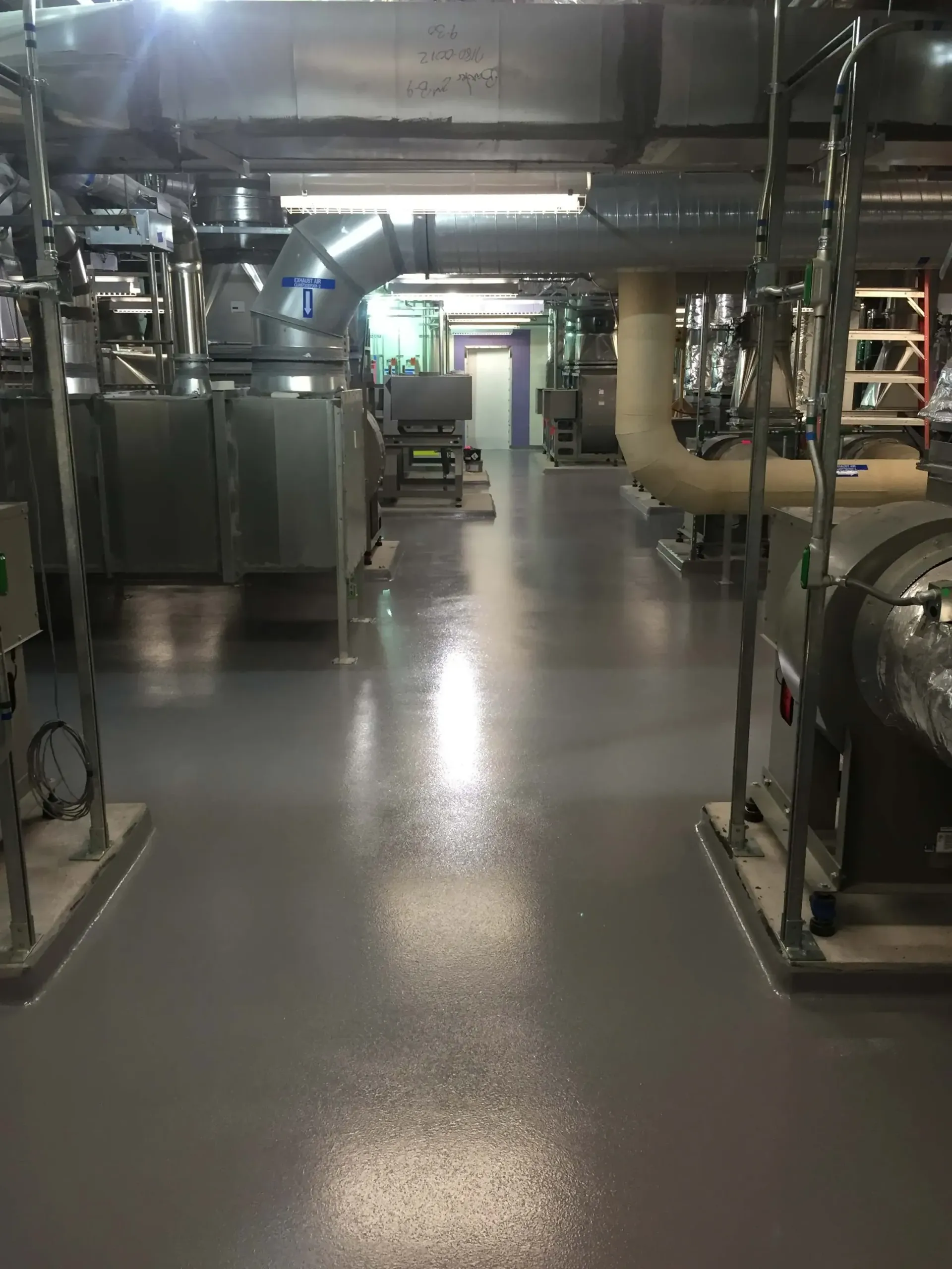 Gray industrial floor with metal equipment and ductwork. Dimly lit, possibly a factory.