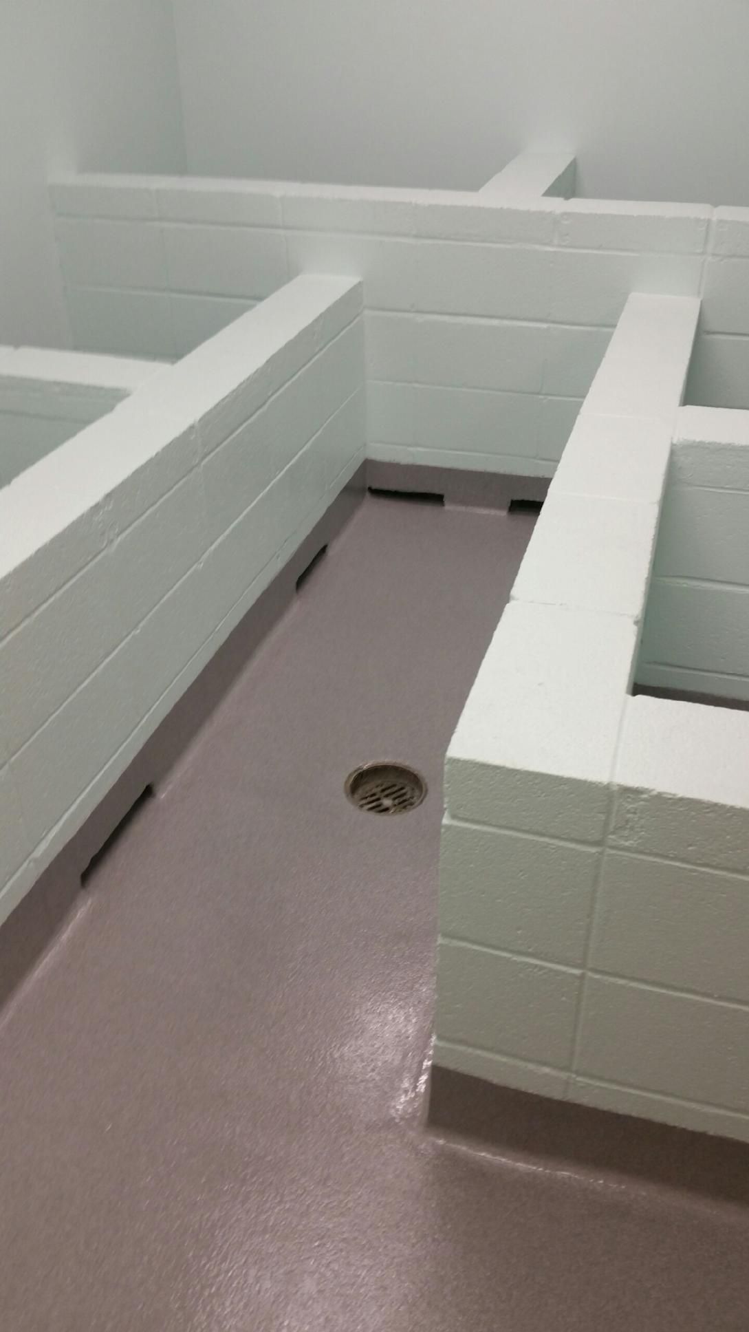 A bathroom with white tiles and a drain in the floor.