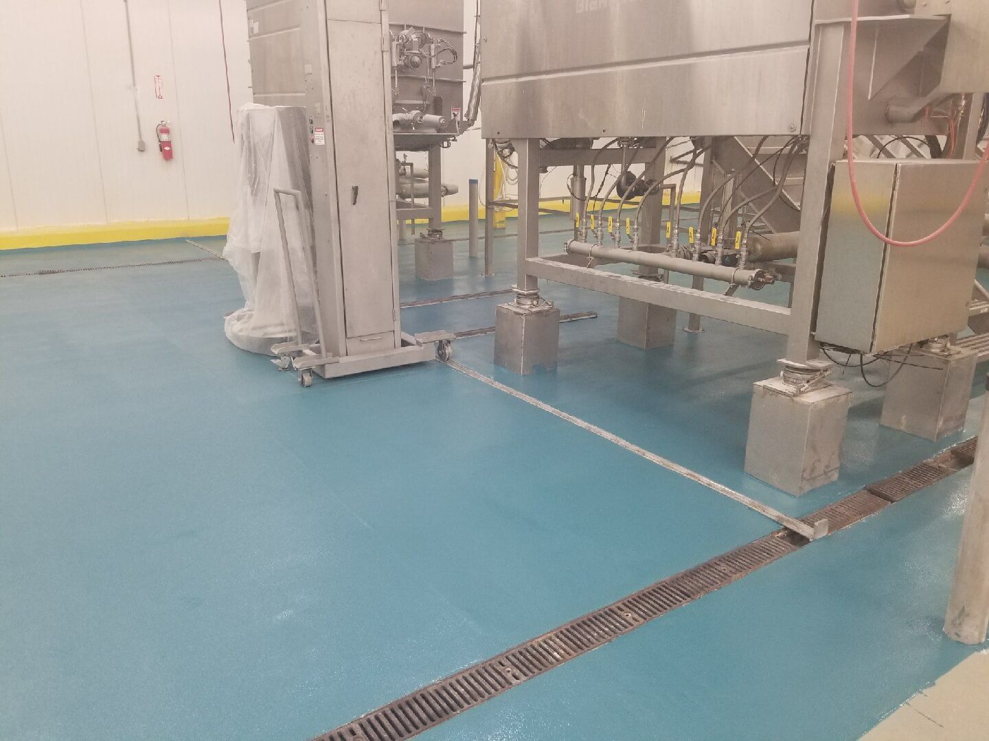 A stainless steel machine is sitting on top of a blue floor in a factory.
